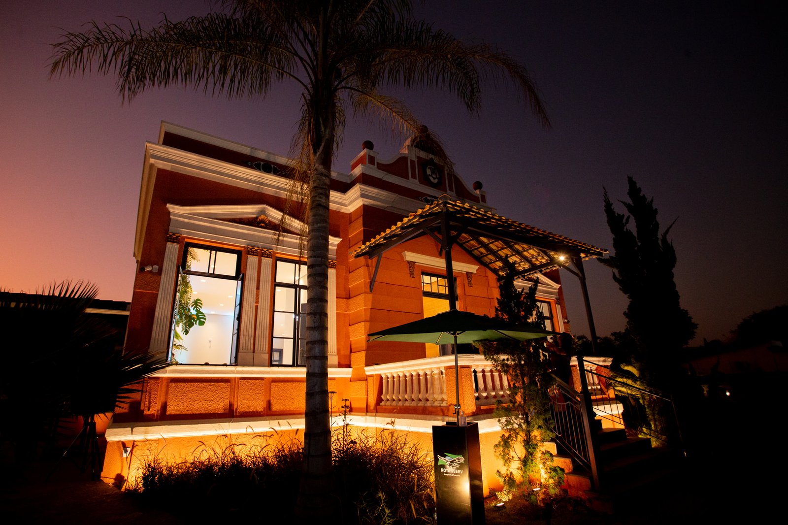 Casarão iluminado à noite com palmeira em primeiro plano