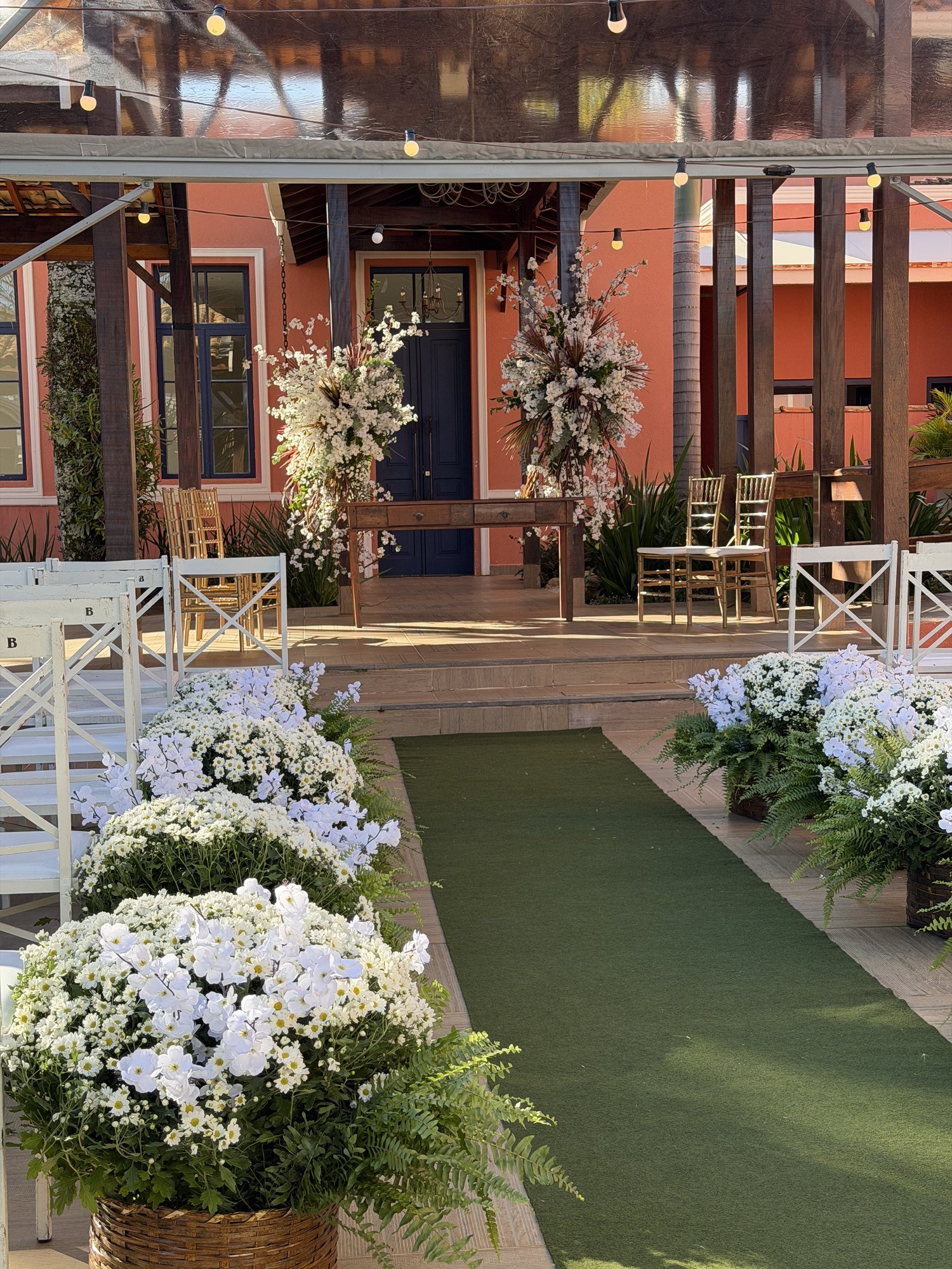 Corredor de cerimônia com arranjos florais brancos e casarão ao fundo